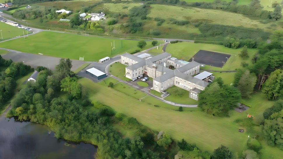 Un panorama rural con edificios de piedra tradicionales y campos verdes en el terreno de Colaiste Mhuire (Tourmakeady).