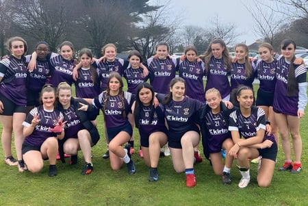 Un grupo de jóvenes futbolistas posan en el campo de la Colaiste Muire Mathair con camisetas moradas.