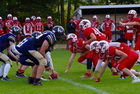 Estudiantes del Collège de Sainte-Anne-de-la-Pocatière juegan un partido de fútbol en el campo deportivo con árboles de fondo.