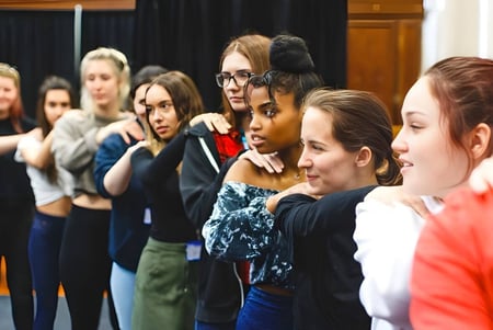 Estudiantes del College of Richard Collyer en un ensayo frente a un telón oscuro.