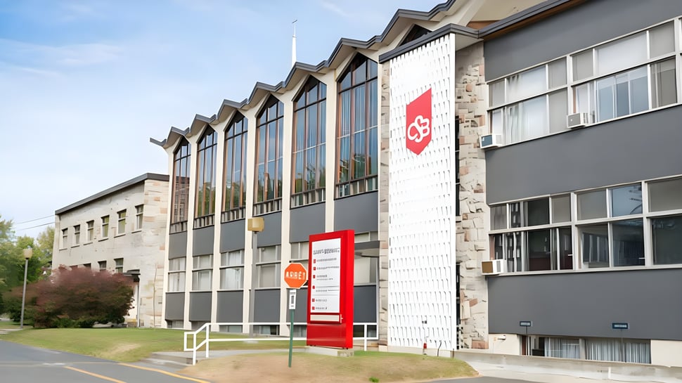 El edificio de varios pisos con grandes ventanas y un logo rojo en el campus del College Saint-Bernard está rodeado de un área verde.