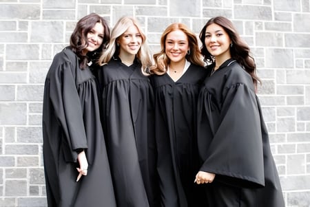 Cuatro estudiantes en togas de graduación negras están de pie frente a una pared de ladrillos grises en el terreno del College Saint-Bernard.