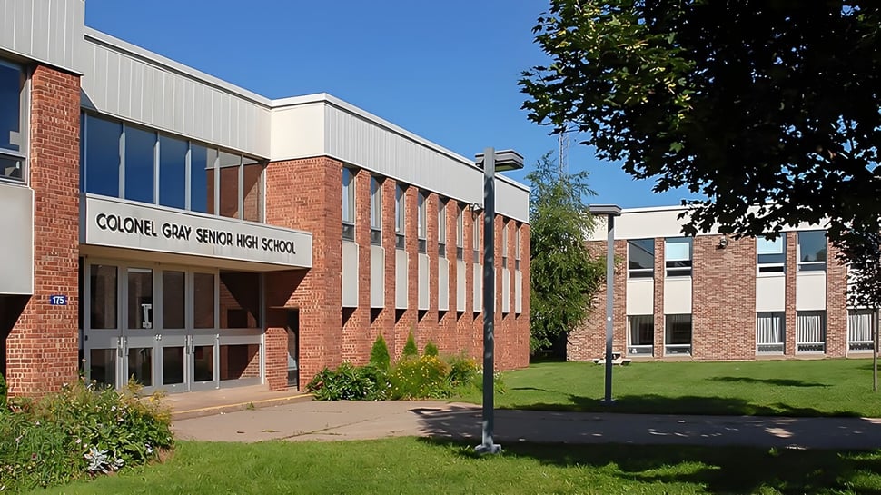 El edificio de ladrillo de varios pisos de la Colonel Gray High School con grandes ventanas y una superficie de césped en el frente.
