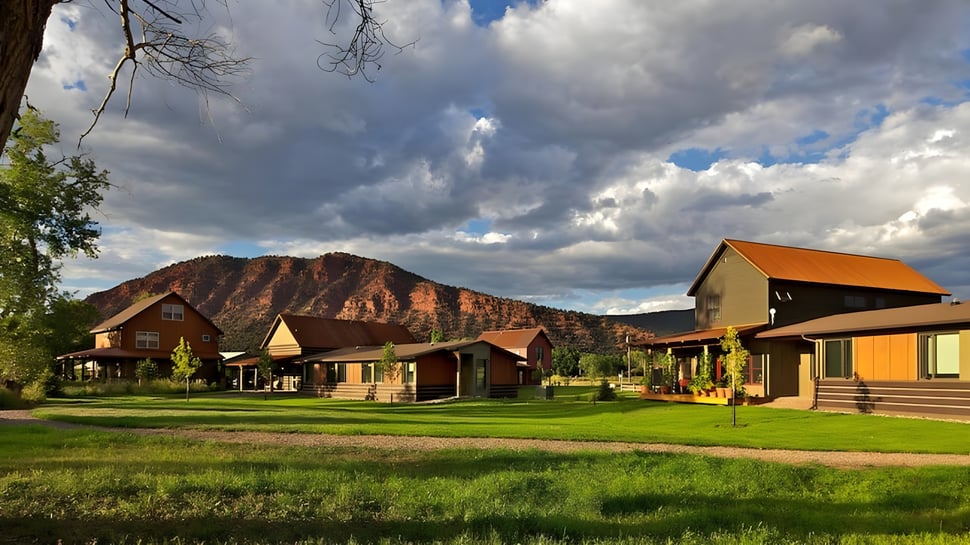 Cabañas rústicas en un paisaje rural con campo cubierto de hierba y montañas al fondo en el terreno de la Colorado Rocky Mountain School.