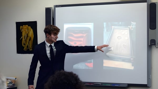 Un hombre en traje está frente a una gran pantalla de proyección y muestra algo en la Colorado Rocky Mountain School.