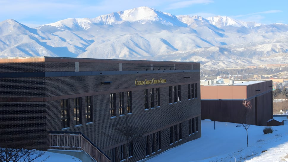 Un moderno edificio de varios pisos de la Colorado Springs Christian School con montañas nevadas al fondo.