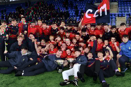 Un grupo de estudiantes del Columba College en uniformes rojos se reúne en el campo deportivo con una bandera roja.