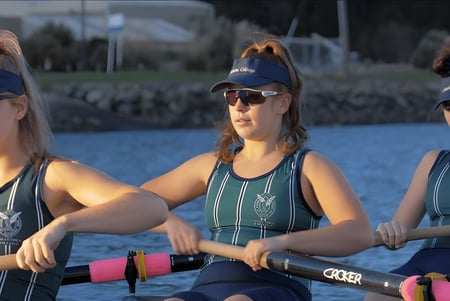 Tres alumnas en trajes de baño están en un muelle frente a una superficie de agua en el campus del Columba College.