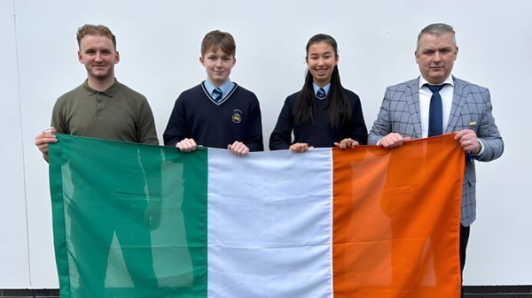Cuatro personas sostienen la bandera irlandesa frente a un fondo blanco en el campus del Comeragh College.
