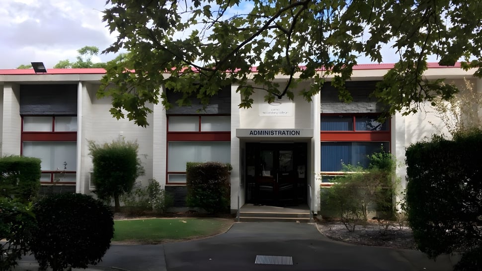 El edificio administrativo con techo rojo y área de entrada en el campus del Como Secondary College está rodeado de árboles.