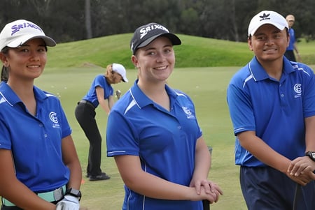 Tres estudiantes en uniformes azules están en el campo de golf del Como Secondary College frente a árboles.