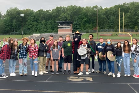 Un grupo de estudiantes está en el campo de deportes de la Comstock Park High School junto a equipos deportivos y árboles.