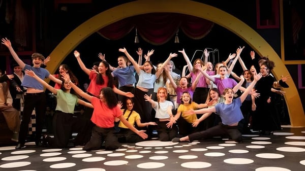 Un grupo de estudiantes vestidos de colores realiza una actuación en el escenario de la Concord Academy ante un gran arco.