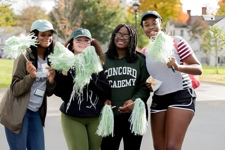 Un grupo de cuatro estudiantes sonríe afuera en el campus de la Concord Academy.