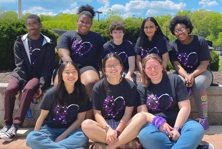 Un grupo de estudiantes de la Connecticut IB Academy posan juntos frente a un fondo de árboles al aire libre.