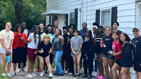 Un grupo de estudiantes está frente al edificio de la Connecticut IB Academy con un entorno verde de fondo.