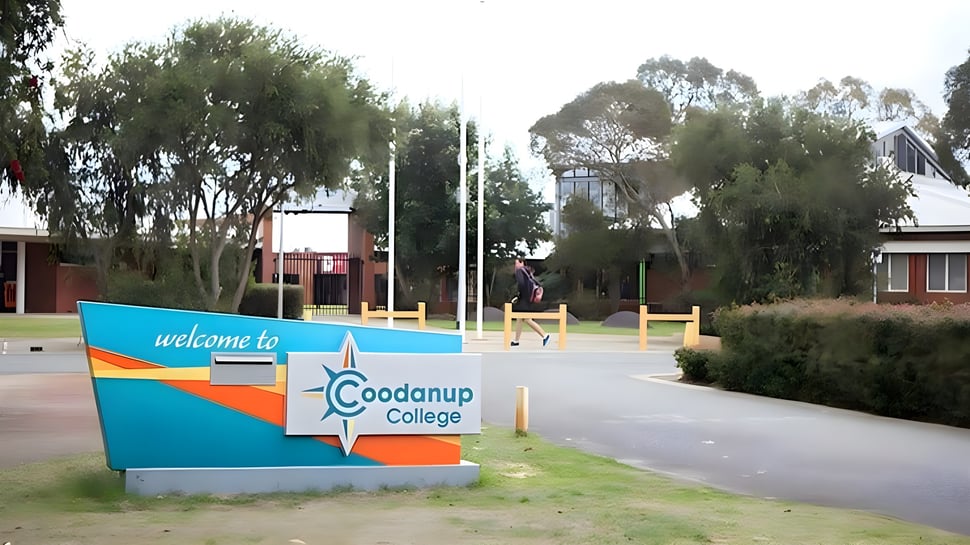 Un colorido cartel de bienvenida se encuentra frente al Coodanup College rodeado de exuberante vegetación y árboles.