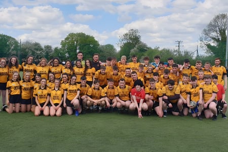 Un gran grupo de alumnas en uniformes amarillos posan para una foto grupal en el césped de la Cornafulla National School.
