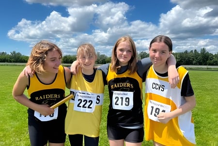 Cuatro jóvenes atletas con camisetas amarillas y negras están en el campo deportivo de la Cornwall Collegiate & Vocational School bajo un cielo nublado.