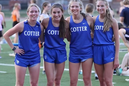 Un grupo de jóvenes atletas de las Cotter Schools está de pie juntos en el campo deportivo.