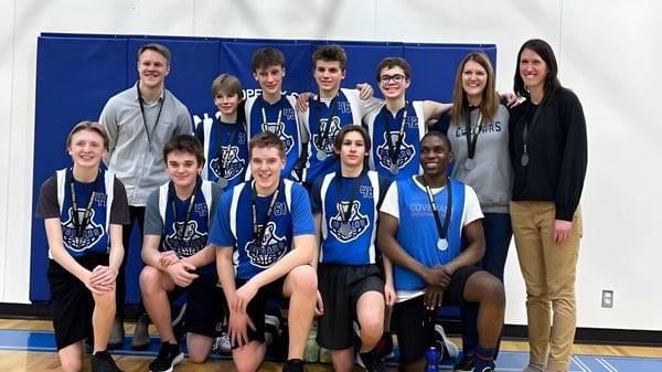 Un grupo de estudiantes de la Covenant Christian School posan juntos como equipo deportivo en un gimnasio frente a un fondo azul.