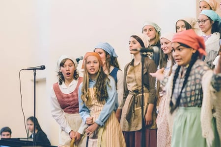 Un grupo de jóvenes mujeres está en el escenario de la Covenant High School con micrófonos durante una actuación.