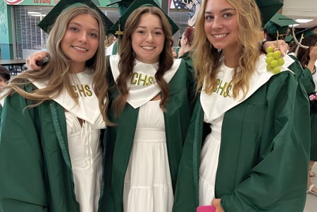 Tres estudiantes en togas de graduación verdes posan juntas para una foto en el campus de Coventry High School.