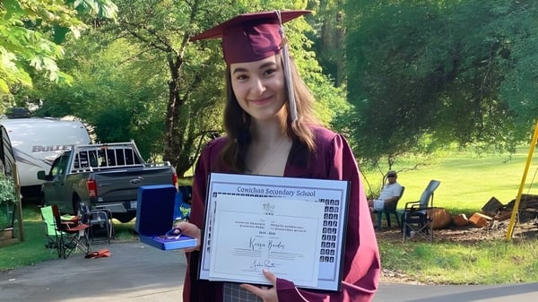 Una graduada de la Cowichan Secondary School está al aire libre con su diploma en la mano.