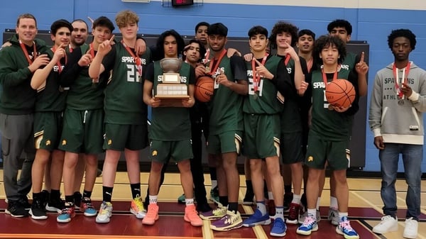 Un grupo de estudiantes de la Craig Kielburger Secondary School posando con un trofeo de baloncesto en el gimnasio.