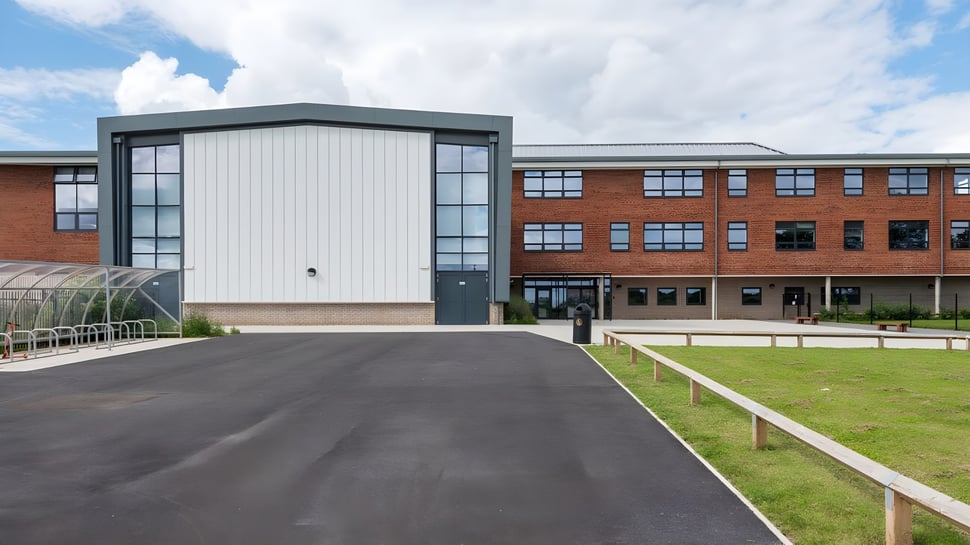 El edificio de ladrillo de varios pisos del Cranbrook Education Campus está rodeado de un campo de césped bajo un cielo azul.