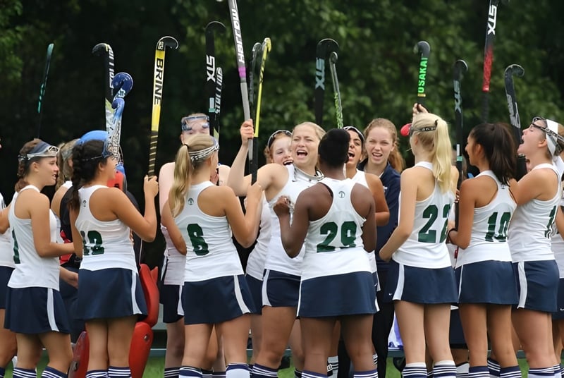 Un grupo de jóvenes tenistas de Cranbrook Schools está junto en la cancha de tenis con raquetas de tenis al fondo.