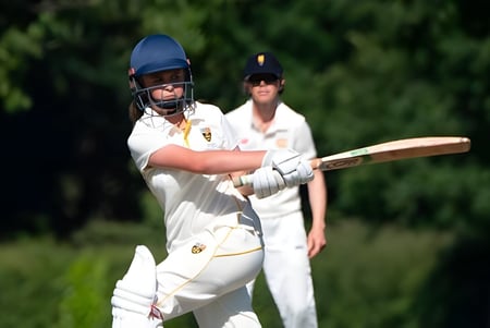Dos jugadores de cricket en uniformes blancos están en el campo de cricket de la Cranleigh School.