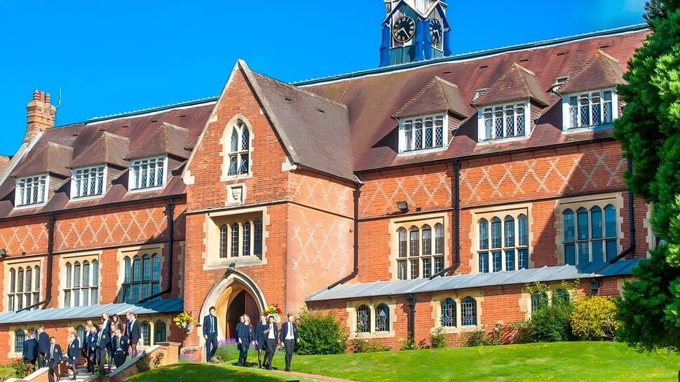 El histórico edificio de ladrillo de la Cranleigh School se encuentra en una zona verde con alumnas y alumnos en primer plano.