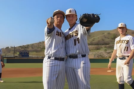 Un grupo de jugadores de béisbol de la Crean Lutheran High School está en uniforme en el campo de béisbol frente a un cielo azul y montañas.