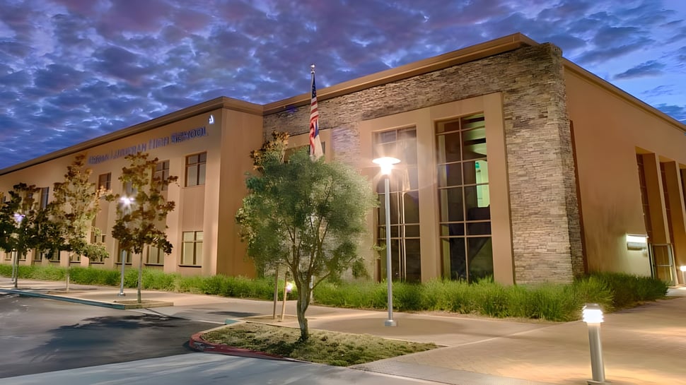 El moderno edificio de varios pisos con fachada de piedra de la Crean Lutheran High School se encuentra frente a un cielo nublado y está rodeado de verde.