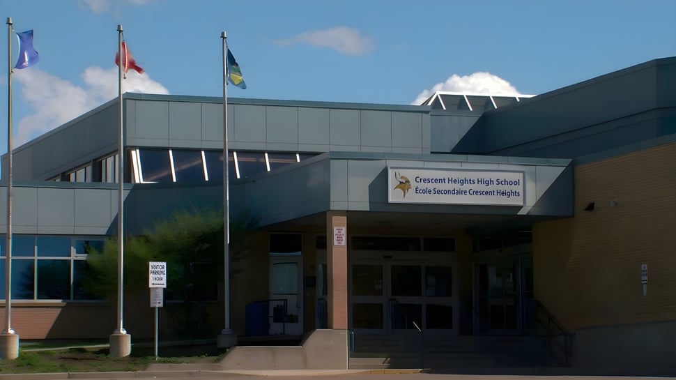 Se puede ver el moderno edificio escolar de la Crescent Heights High School con banderas ondeando en el techo.