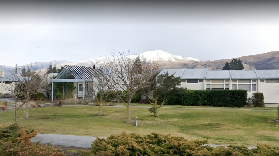 Un parque con un pabellón y árboles en el terreno del Cromwell College frente a montañas cubiertas de nieve en el fondo.