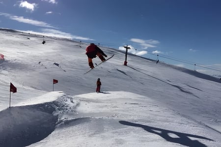 Estudiantes del Cromwell College descienden por una pista de esquí nevada bajo un cielo azul con algunas nubes.