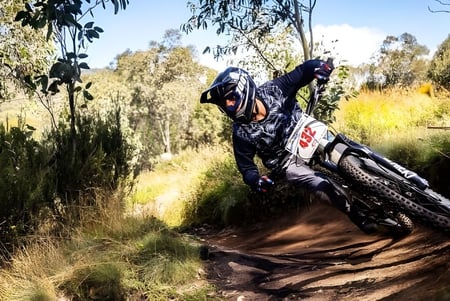 Una persona vestida de camuflaje conduce una dirtbike por un sendero boscoso en el terreno de la Cronulla High School.