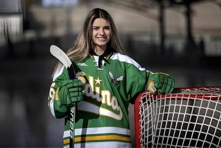 Una estudiante de la Crowsnest Consolidated High School está con un palo de hockey frente a una portería de hockey.
