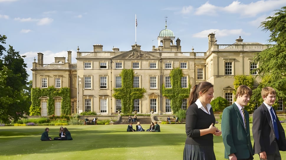 Varias personas en ropa formal se reúnen en el césped frente al edificio histórico de la Culford School.