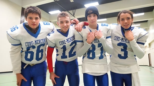 Cuatro estudiantes de la École Polyvalente Secondaire Curé-Mercure posan en el vestuario con camisetas deportivas.