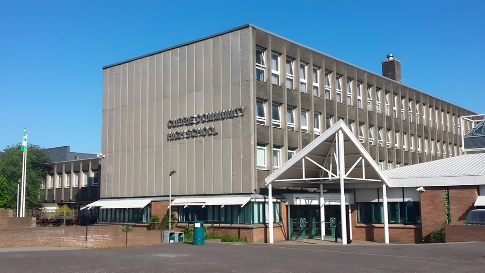El moderno edificio principal de la Currie Community High School con un área pavimentada adyacente y zonas verdes al fondo.