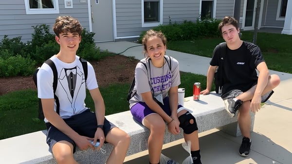 Tres estudiantes están sentados frente a un edificio en una escalera en el campus de la Cushing Academy.