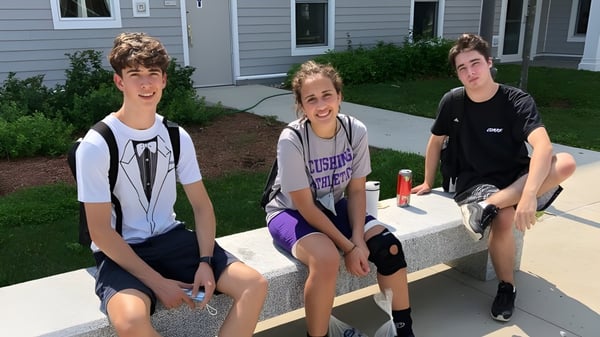 Tres estudiantes están sentados en un escalón frente a un edificio en el campus de la Cushing Academy.