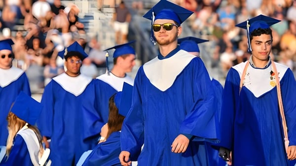 Un grupo de graduados en togas azules del Daniel McIntyre Collegiate Institute camina juntos en una ceremonia de graduación.