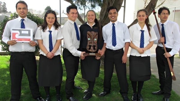 Un grupo de estudiantes en uniformes escolares está de pie juntos en un prado en el terreno de la Dannevirke High School.