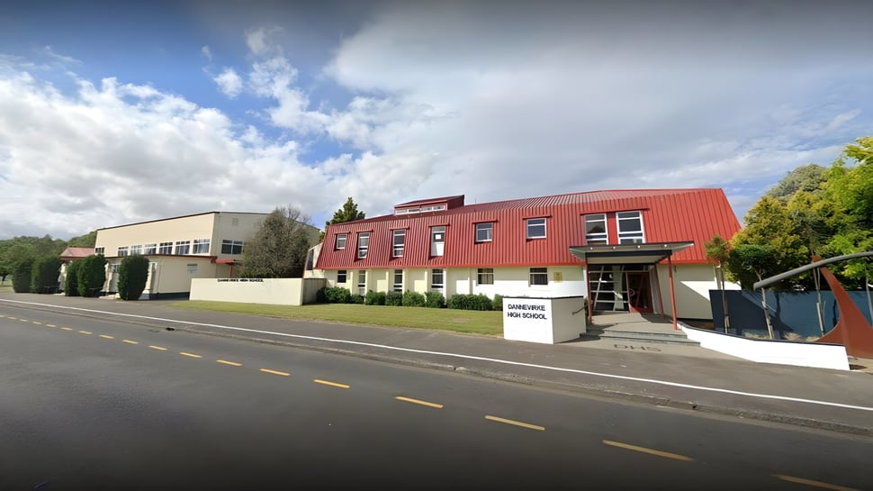 El moderno edificio de varios pisos de la Dannevirke High School con fachada roja está en una calle y está rodeado de árboles.