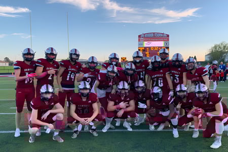 Un grupo de jugadores de fútbol americano con camisetas rojas está reunido en el campo de deportes de la Danville Community High School.