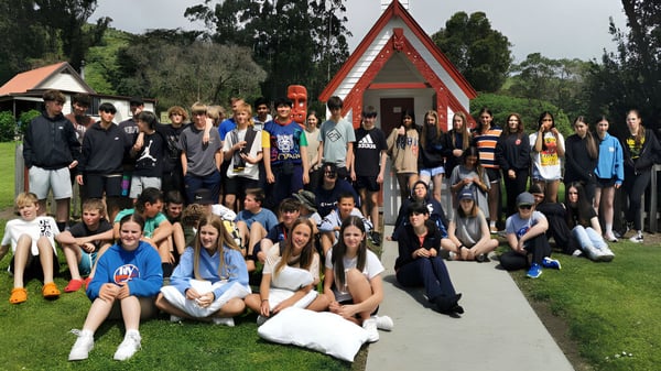 Estudiantes de la Darfield High School se reúnen frente a una casa de reunión tradicional maorí en el campo.